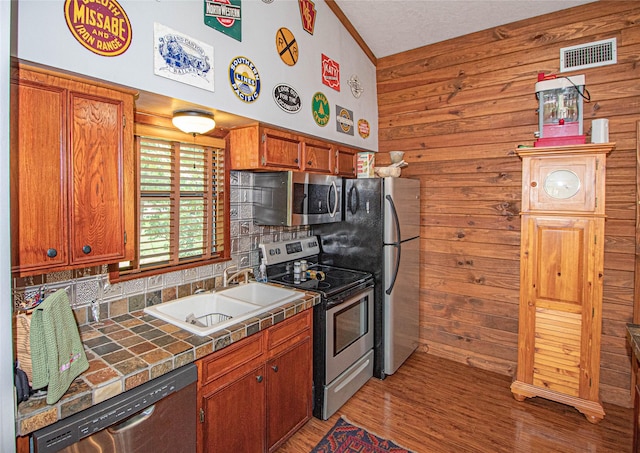 70 Lower Cove Dr, Point Blank, TX 77364 - kitchen featuring stainless steel appliances, a sink, tile counters, wood walls, and light wood-type flooring