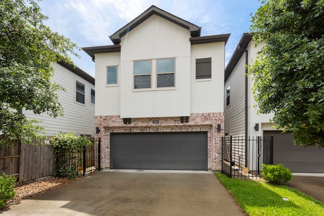 modern home featuring a garage, driveway, brick siding, stucco siding, and fence