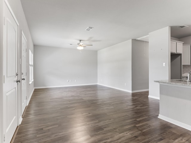 unfurnished living room with a sink, visible vents, ceiling fan, baseboards, and dark wood finished floors
