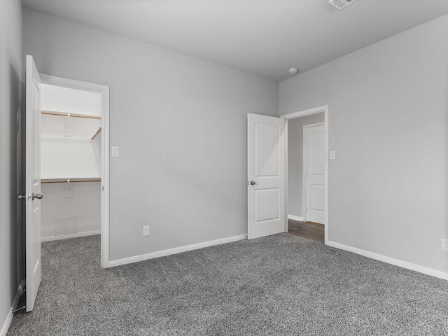 unfurnished bedroom with a walk in closet, baseboards, and carpet floors