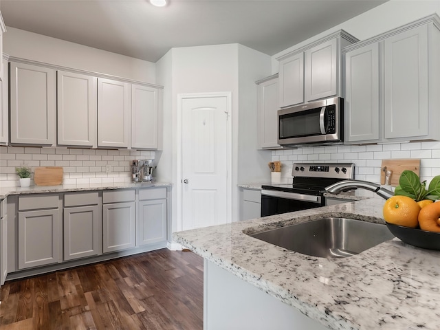 2921 4th St, Bay City, TX 77414 - kitchen featuring appliances with stainless steel finishes, dark wood-style floors, a sink, light stone counters, and decorative backsplash