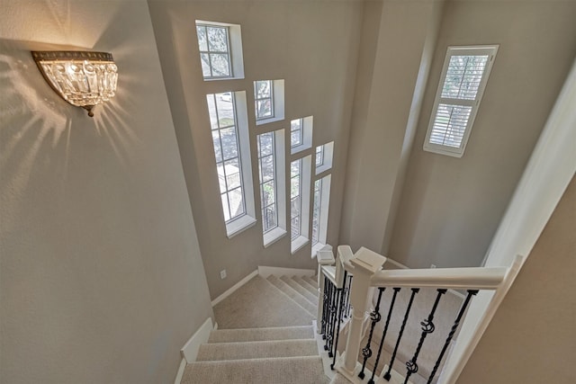 stairway featuring an inviting chandelier, baseboards, a high ceiling, and carpet floors