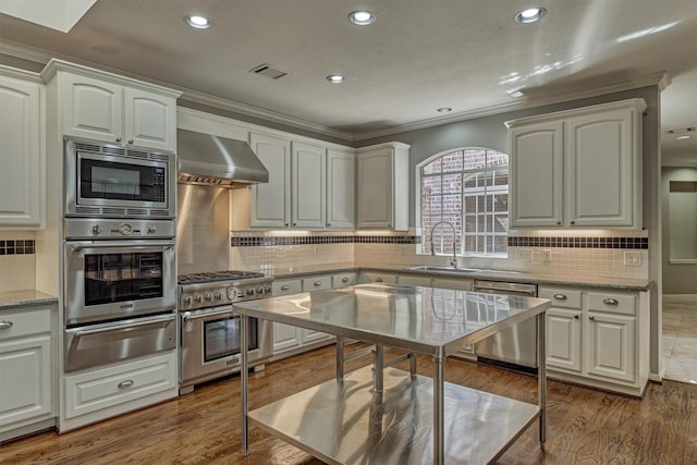kitchen with appliances with stainless steel finishes, a warming drawer, backsplash, a sink, and wall chimney exhaust hood