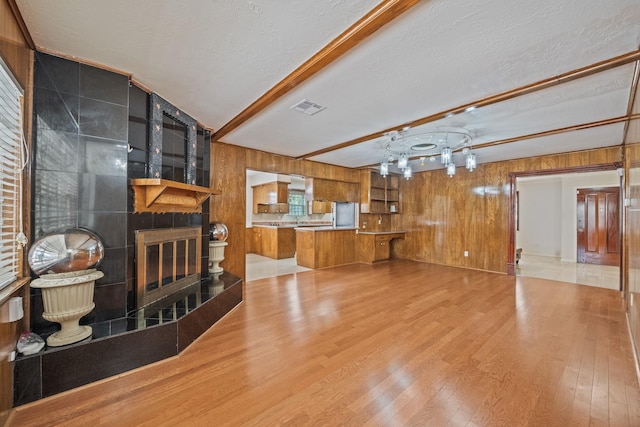 7718 Pella Dr, Houston, TX 77036 - unfurnished living room featuring a tile fireplace, beam ceiling, visible vents, wood walls, and wood finished floors