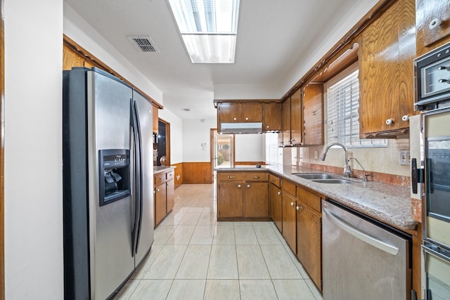 7718 Pella Dr, Houston, TX 77036 - kitchen with brown cabinets, a sink, appliances with stainless steel finishes, visible vents, and a wainscoted wall