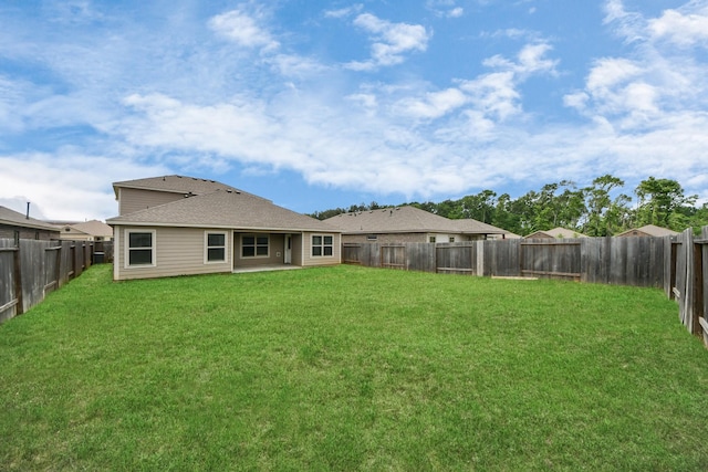 rear view of house featuring a lawn, a fenced backyard, and roof with shingles