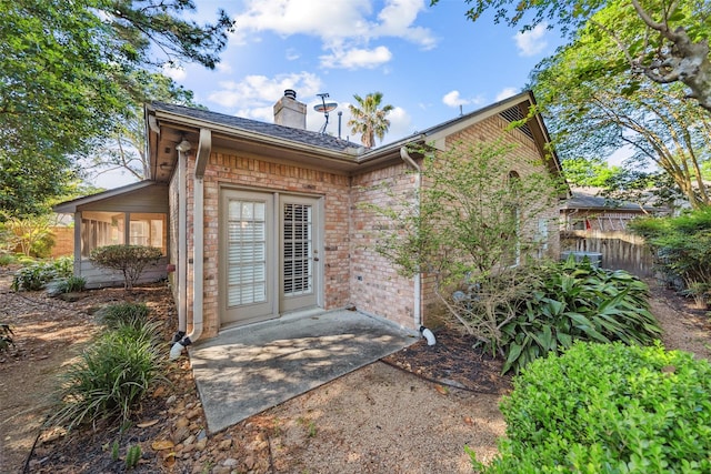 property entrance featuring a patio, brick siding, a chimney, roof with shingles, and fence