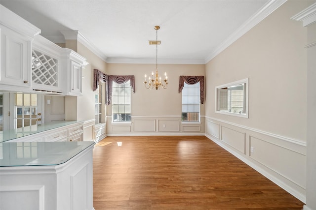 unfurnished dining area featuring a chandelier, ornamental molding, light wood finished floors, and a decorative wall