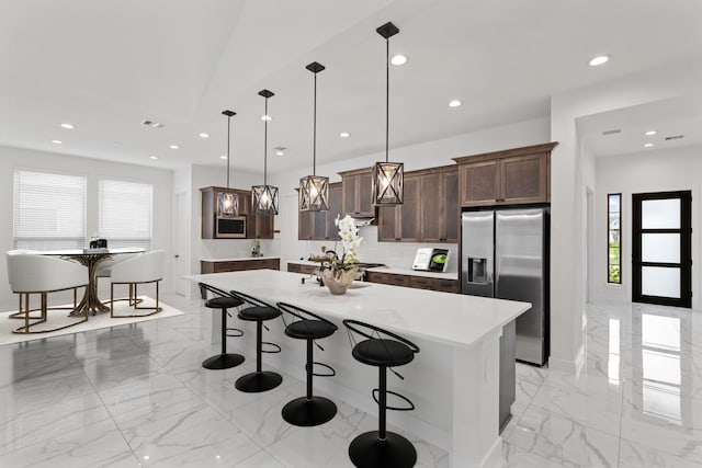 kitchen with marble finish floor, a kitchen island, a kitchen breakfast bar, light countertops, and stainless steel fridge with ice dispenser