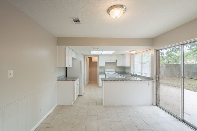 kitchen featuring dark stone counters, white appliances, a sink, under cabinet range hood, and a peninsula