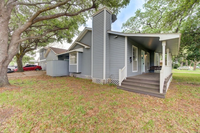 view of side of home with a porch, a lawn, and a chimney
