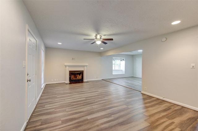 unfurnished living room featuring a fireplace with flush hearth, baseboards, recessed lighting, light wood finished floors, and a ceiling fan