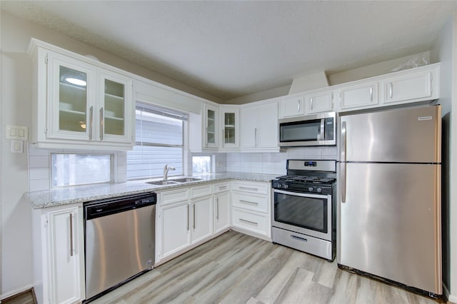 kitchen with appliances with stainless steel finishes, white cabinetry, light wood finished floors, and a sink