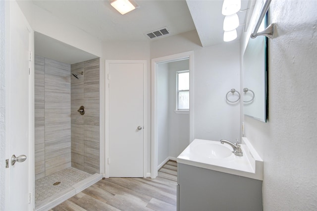 full bathroom with wood finished floors, visible vents, vanity, and tiled shower