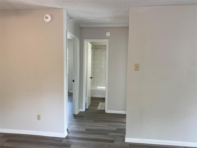 corridor featuring a textured ceiling, dark wood finished floors, and baseboards