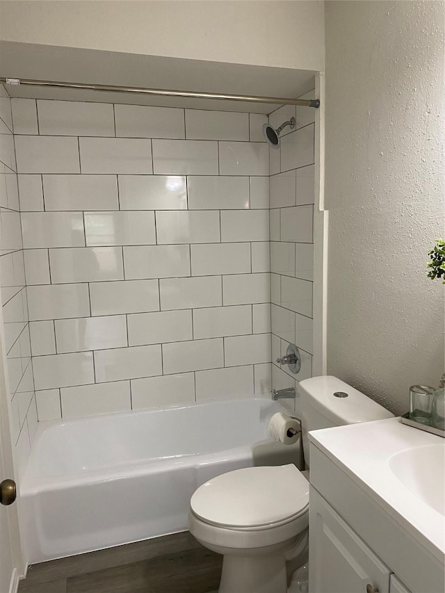 bathroom featuring washtub / shower combination, a textured wall, toilet, wood finished floors, and vanity