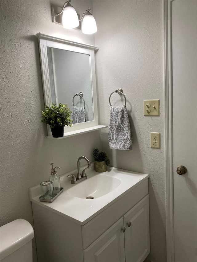 half bathroom with toilet, a textured wall, and vanity