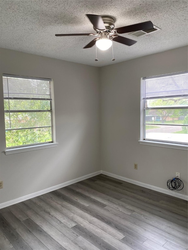 spare room featuring visible vents, wood finished floors, a healthy amount of sunlight, and ceiling fan