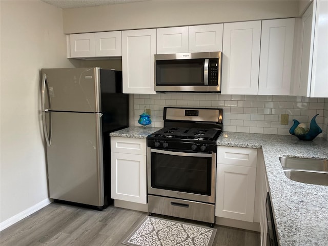 kitchen featuring light wood-style flooring, appliances with stainless steel finishes, decorative backsplash, and white cabinetry
