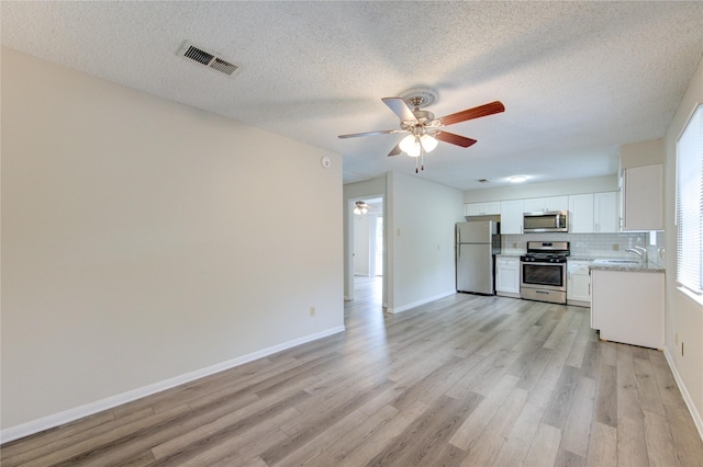 112 Begonia Ln, Highlands, TX 77562 - kitchen with appliances with stainless steel finishes, a ceiling fan, light wood finished floors, white cabinetry, and tasteful backsplash