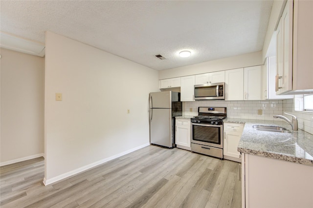 112 Begonia Ln, Highlands, TX 77562 - kitchen featuring appliances with stainless steel finishes, a sink, light wood-style flooring, backsplash, and a textured ceiling