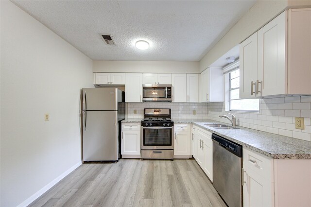 112 Begonia Ln, Highlands, TX 77562 - kitchen featuring appliances with stainless steel finishes, a sink, light wood-type flooring, decorative backsplash, and a textured ceiling