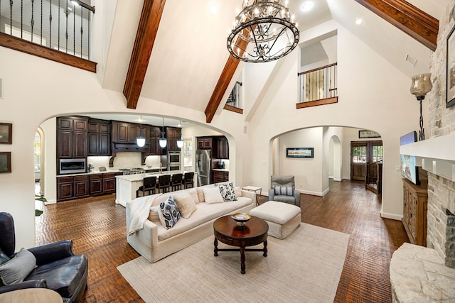 living room with an inviting chandelier, arched walkways, high vaulted ceiling, and beamed ceiling