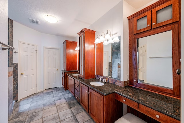 full bath with a sink, stone finish flooring, a tile shower, double vanity, and visible vents