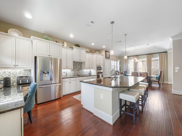 kitchen with a sink, decorative backsplash, a kitchen bar, visible vents, and appliances with stainless steel finishes