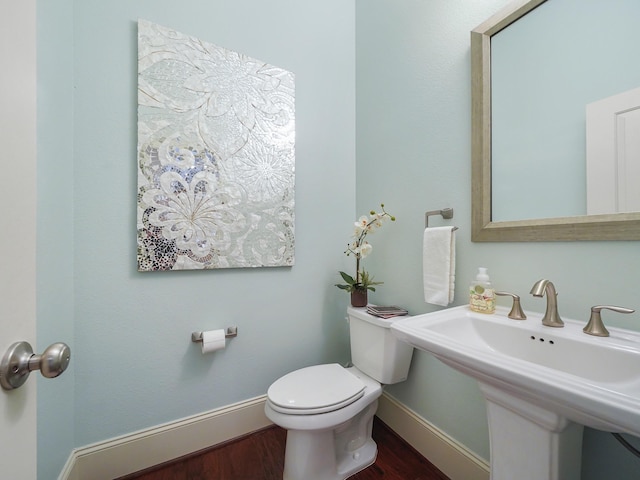 half bathroom with toilet, a sink, wood finished floors, and baseboards