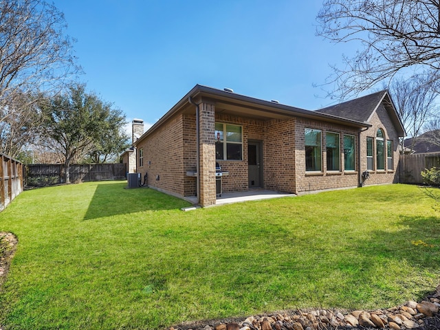 rear view of house with a fenced backyard, a yard, brick siding, a patio, and central AC