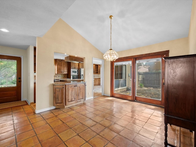 kitchen with an inviting chandelier, brown cabinetry, stainless steel microwave, baseboards, and vaulted ceiling