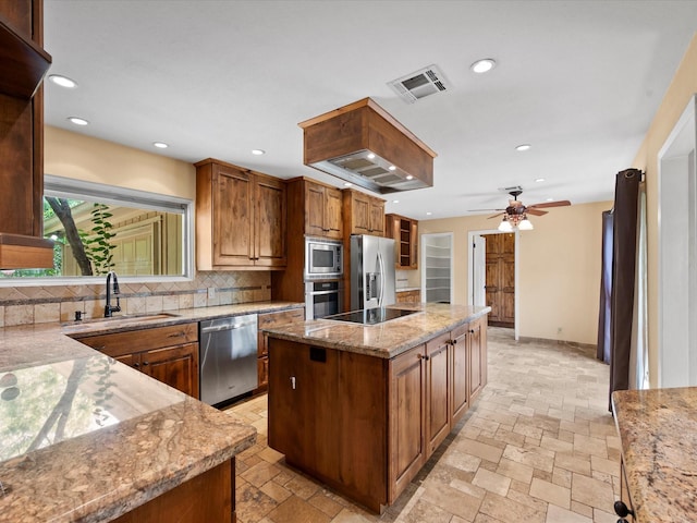 kitchen with light stone countertops, a sink, a center island, stainless steel appliances, and decorative backsplash