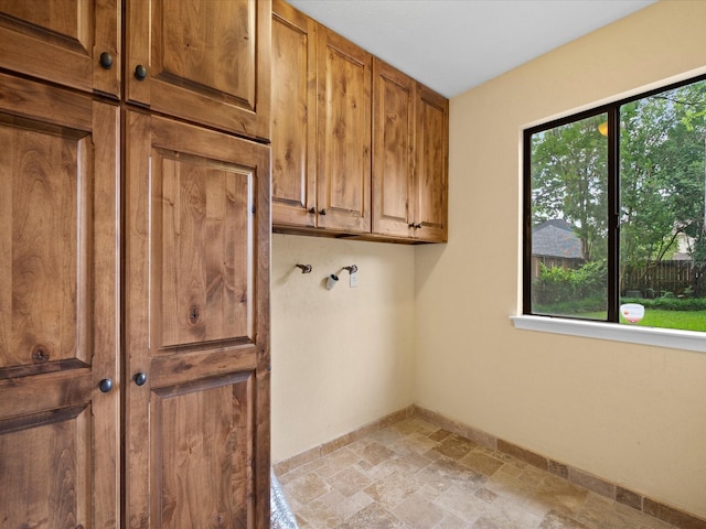 laundry room featuring cabinet space, baseboards, and stone finish floor