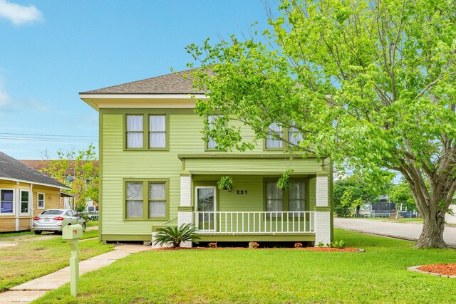 view of front of property featuring covered porch, a front lawn, and roof with shingles