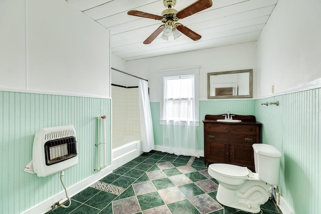 full bathroom with a wainscoted wall, heating unit, toilet, shower / bath combination with curtain, and a ceiling fan