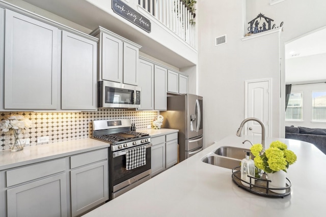 kitchen featuring stainless steel appliances, a sink, visible vents, backsplash, and light countertops