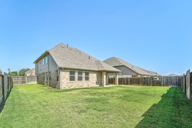 rear view of house featuring a lawn, a shingled roof, a fenced backyard, and brick siding