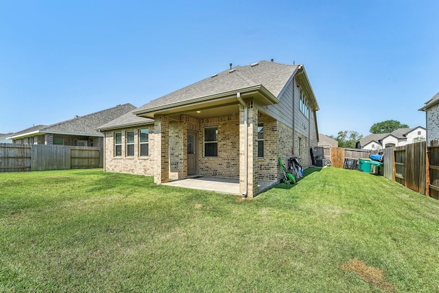 rear view of property with a fenced backyard, brick siding, a shingled roof, a patio, and a lawn