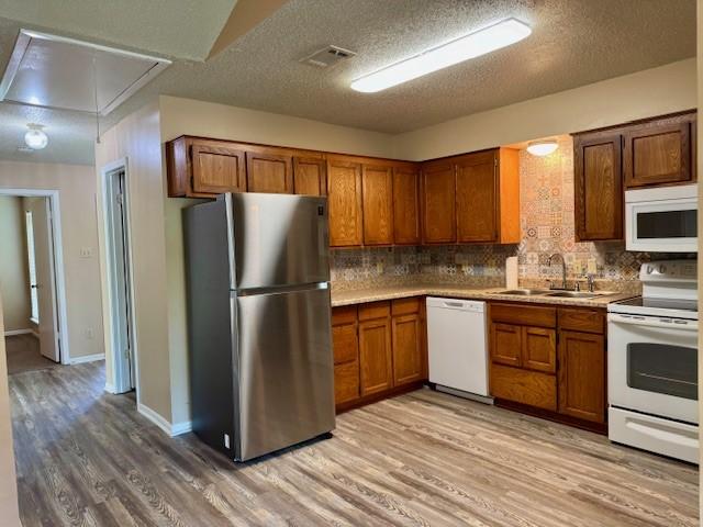 kitchen featuring white appliances, brown cabinets, light wood finished floors, and a sink