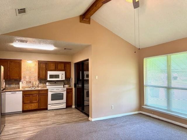 kitchen with a sink, lofted ceiling with beams, white appliances, tasteful backsplash, and baseboards