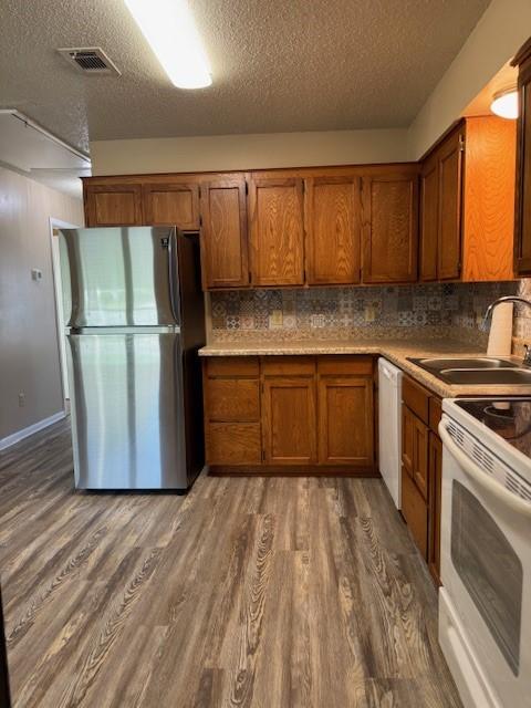 kitchen with a textured ceiling, visible vents, wood finished floors, white appliances, and brown cabinetry