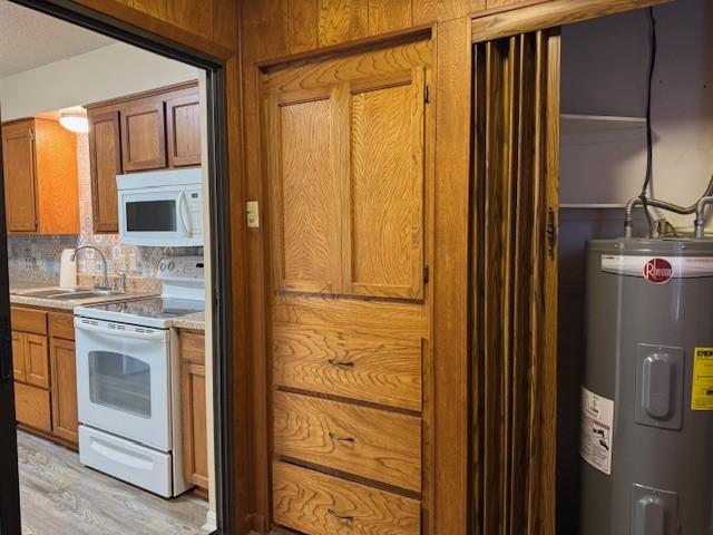 kitchen featuring a sink, brown cabinets, white appliances, water heater, and light countertops