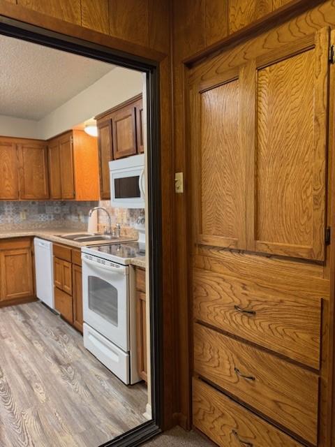 kitchen featuring white appliances, light countertops, brown cabinets, backsplash, and a sink