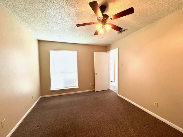 spare room with visible vents, dark carpet, ceiling fan, and a textured ceiling