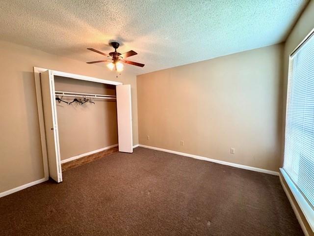 unfurnished bedroom with a closet, ceiling fan, dark colored carpet, and a textured ceiling