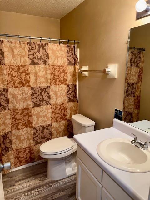 bathroom with a textured ceiling, a shower with shower curtain, toilet, wood finished floors, and vanity