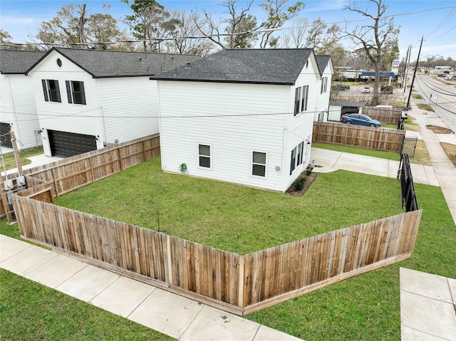 view of side of home featuring an attached garage, fence private yard, a yard, and roof with shingles