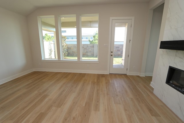 unfurnished living room with a high end fireplace, baseboards, lofted ceiling, and light wood-style floors