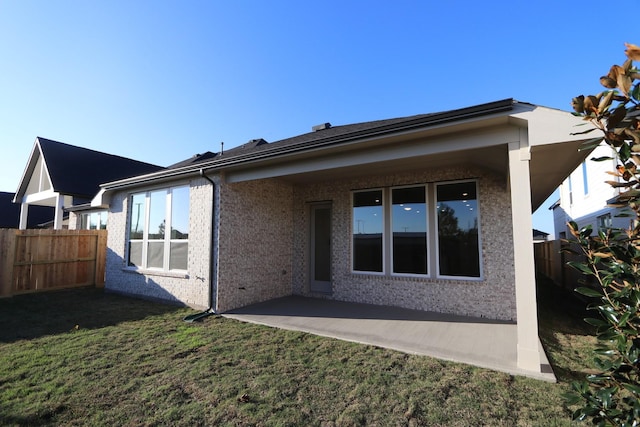 rear view of property featuring a patio, brick siding, fence, and a yard